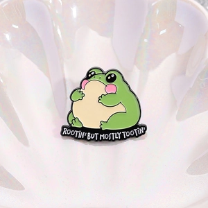 Cute green enamel frog brooch with Rootin' But Mostly Tootin' slogan on shell background