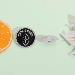 Minimalist geometric S-shaped brooch and Cool S Crew badge on a fresh green background