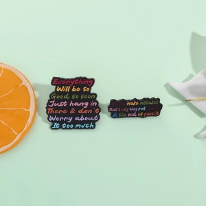 Bunte Emaille-Pins mit Zitaten auf schwarzem Grund vor minzgrünem Hintergrund