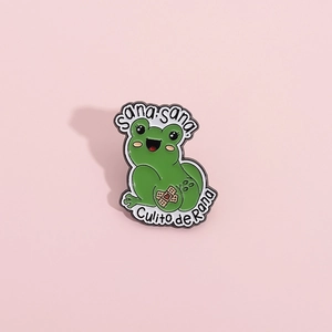 Funny green frog enamel pin featuring Sana sana Culito de Rana text on pink background