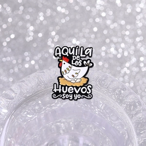 Cartoon hen laying eggs enamel pin with Spanish text on a sparkling silver background
