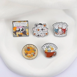 Cinq broches en émail sur le thème des chats, Catpuccino et Cat Mom, sur un plateau blanc
