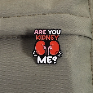 Close-up of Are You Kidney Me? enamel pin on green canvas bag for medical theme decor