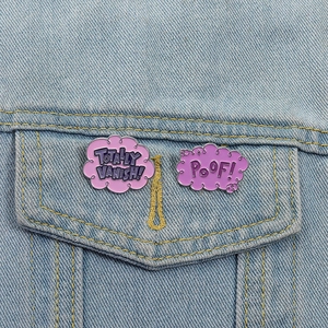 Détail de pins en émail violet en forme de nuage avec texte POOF sur veste en jean