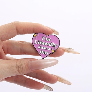 Detail of pink heart enamel pin with white lettering held in hand on white backdrop