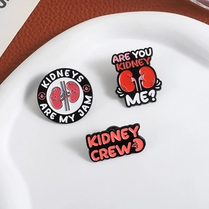 Three cartoon kidney enamel pins with funny slogans on a white ceramic plate background