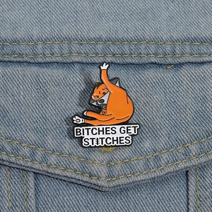 Funny orange cat enamel pin wearing medical collar on blue denim fabric background