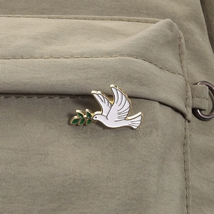 Detailed view of a white dove enamel pin with a green olive branch on khaki fabric