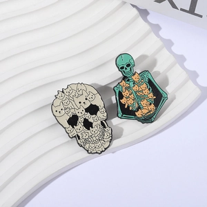 Detail of gothic enamel pins featuring white cats skull and green skeleton with orange cats
