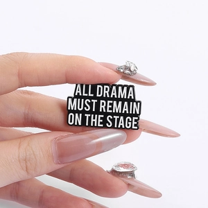 Black enamel brooch with 'ALL DRAMA MUST REMAIN ON THE STAGE' text and metal trim