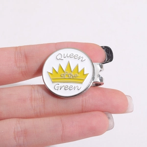 Détail d'un marqueur de golf avec couronne jaune et texte Queen of the Green sur émail blanc