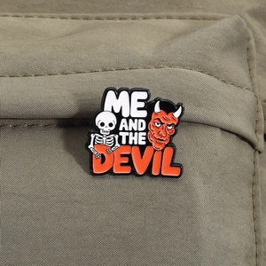 Detail of Me and the Devil enamel pin featuring a skull and red demon on canvas bag