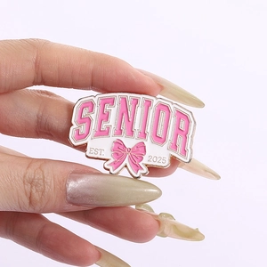 Close-up of pink enamel Senior 2025 graduation brooch with bow detail and bold lettering