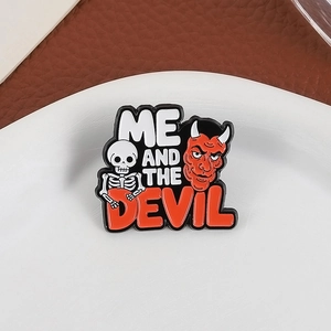 Cartoon enamel pin featuring a white skull and red devil with Me And The Devil text