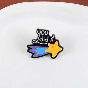 Detail of a comet star enamel pin featuring a smiling face and 'YOU did it' text