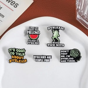 Vue détaillée de cinq broches en émail colorées sur la dyslexie posées sur un plat en céramique