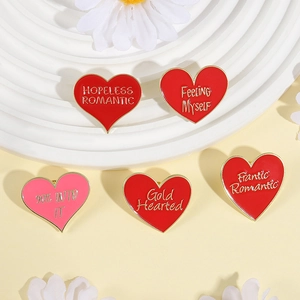 Dettaglio di cinque spille in smalto a cuore con bordo dorato e scritte romantiche inglesi
