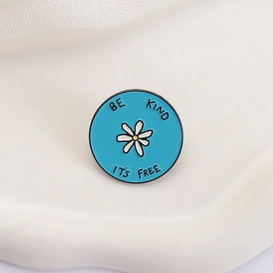 Detail of blue enamel flower brooch with Be Kind It's Free text on white pedestal