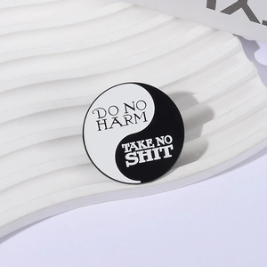 Geometrische Yin-Yang-Emaille-Anstecknadel mit Text auf einem weißen Display-Tablett