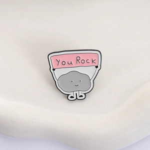 Macro shot of stone cartoon enamel pin featuring You Rock banner on gray background