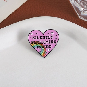 Rainbow heart enamel pin with Silently Screaming Inside text on white plate