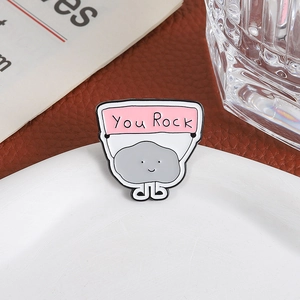 Creative enamel pin featuring a cute rock holding a You Rock banner on white ceramic