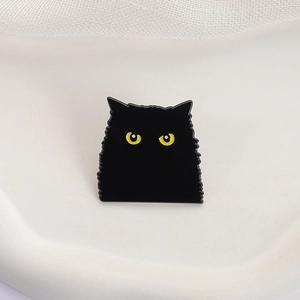 Dettaglio di una spilla smaltata a forma di gatto nero con occhi gialli su vassoio