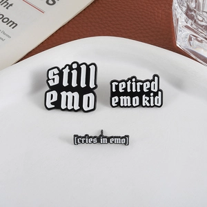 Three-piece black and white enamel pin set with emo theme text on a white ceramic plate