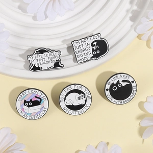 Five cartoon black and white cat enamel pins with funny quotes on a white tiered stand