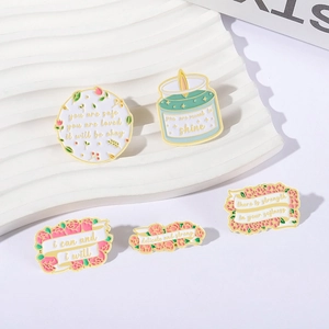 Set of 5 colorful enamel flower badges with motivational quotes on a white display stand