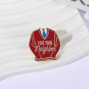 Macro view of red sweater enamel pin with Love Your Neighbor text and gold trim