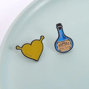 Cartoon green heart monster and blue potion enamel pins on ceramic surface