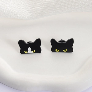 Minimalist black enamel cat earrings with yellow eyes on a white stone display stand