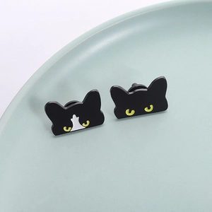 Cute black cat enamel pins with bright yellow eyes displayed on a ceramic tray