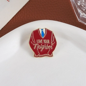 Red sweater enamel pin featuring LOVE YOUR Neighbor quote on a white ceramic plate