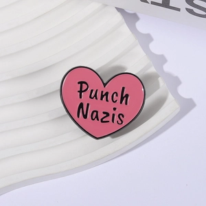 Pink heart-shaped enamel pin with Punch Nazis text on a white textured background