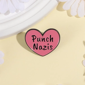 Close-up of pink heart enamel pin with Punch Nazis text on light beige background