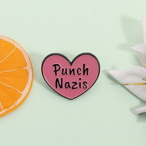 Pink heart enamel pin with Punch Nazis text and black metal trim on a teal background