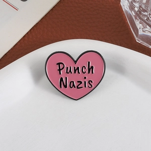 Pink heart-shaped enamel pin with Punch Nazis slogan on a white ceramic plate