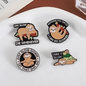 Set of four cute cartoon sloth enamel pins on a white tray with leather background