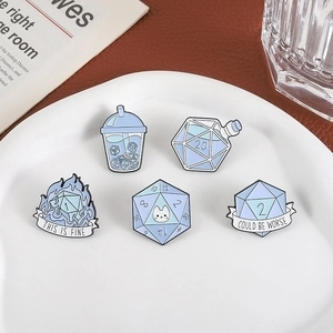 Set of 5 light blue enamel pins featuring dice and DND themes on a white ceramic plate