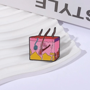 Cartoon skin anatomy enamel pin showing dermal layers and follicles on a white tray
