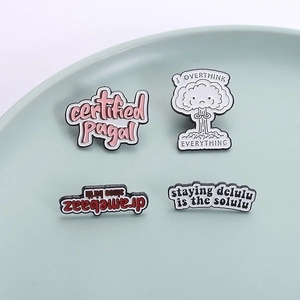 Set mit vier kreativen Metall-Emaille-Pins mit lustigen Sprüchen auf einem Keramikteller