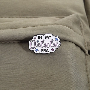 Détail d'un pin's en émail en forme de nuage avec texte sur un tissu vert