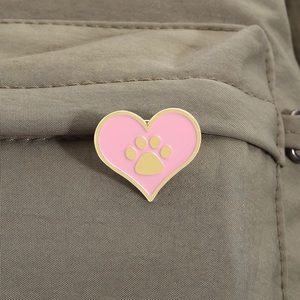 Gros plan sur un pin's cœur rose en émail avec empreinte dorée sur un sac en toile