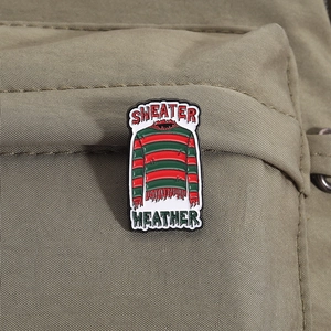 Détail macro du pin's émaillé pull d'horreur à rayures rouges et vertes sur sac
