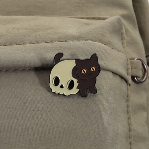 Gros plan d'un pin's en émail chat noir et crâne sur un sac en toile vert olive