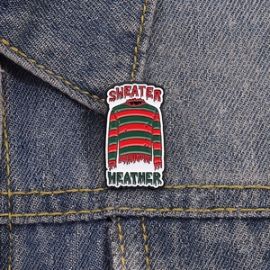 Gros plan d'un pin's émaillé pull d'horreur à rayures rouges et vertes sur denim