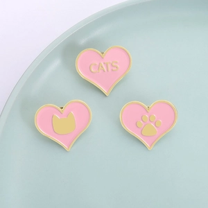 Trois badges de chat en émail rose en forme de cœur avec bordure dorée sur plateau