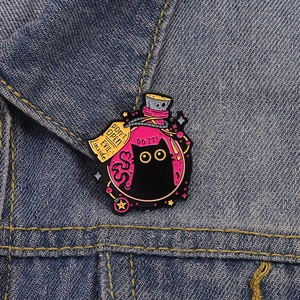 Detail of enamel pin with black cat in pink potion bottle on denim jacket fabric